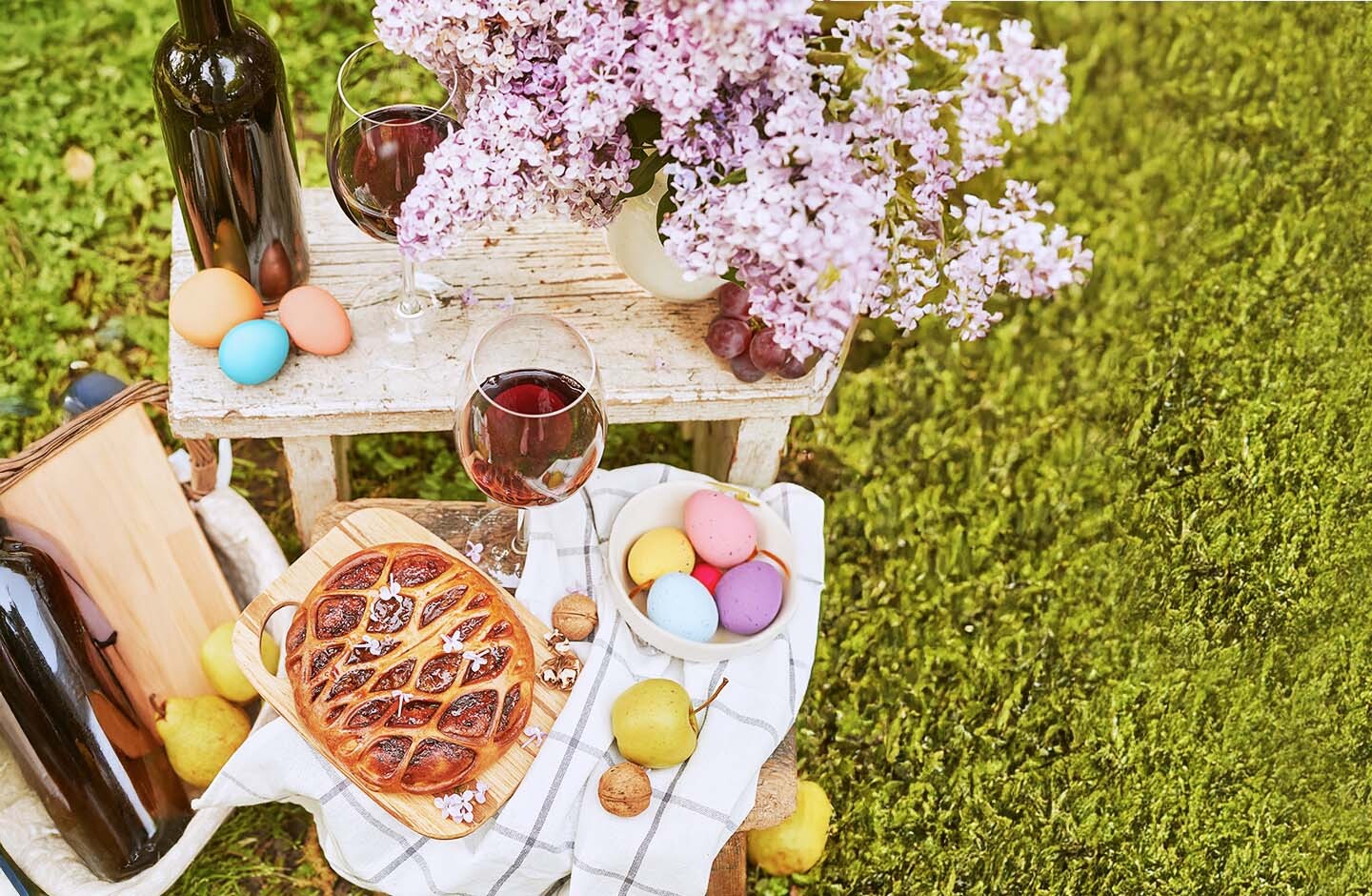 Bicchiere di vino rosso su tavolino da picnic con uova colorate e cesto – idea per Pasqua e Pasquetta all’aperto