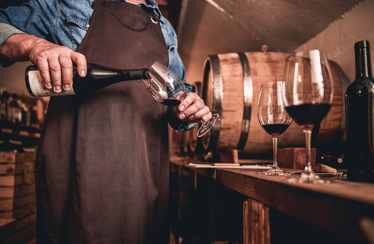 Sommelier versa vino rosso in cantina con botti sullo sfondo