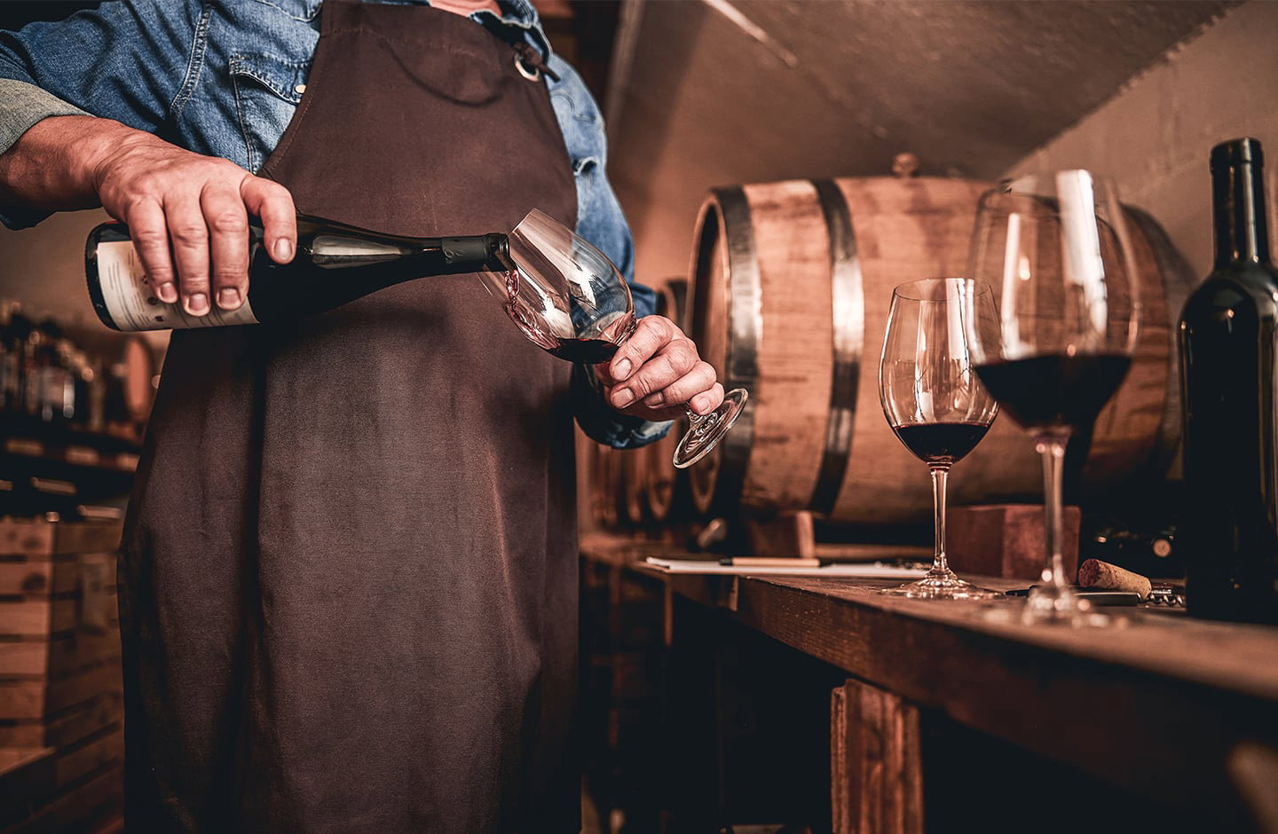 Sommelier versa vino rosso in cantina con botti sullo sfondo
