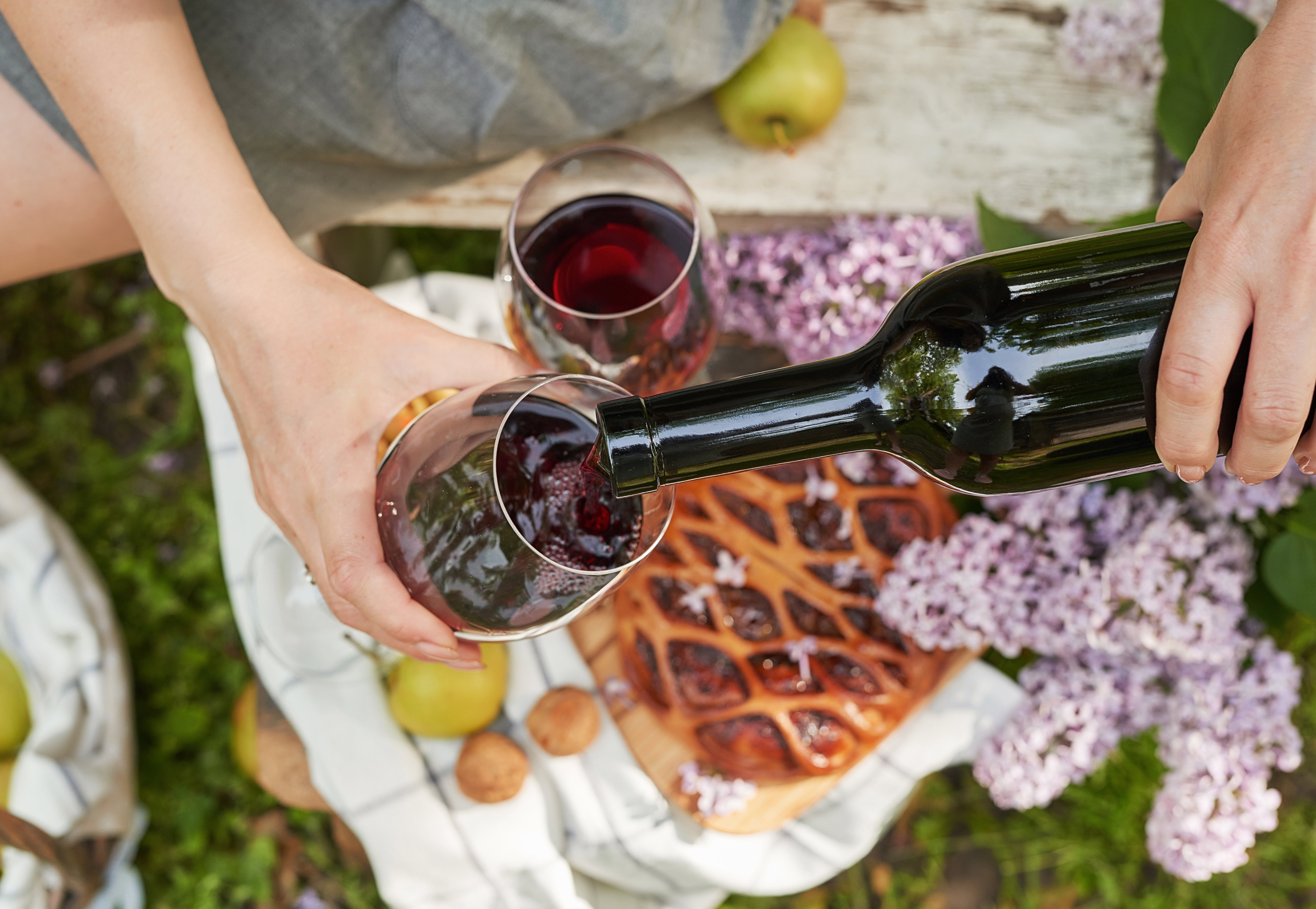Versare vino dolce rosso in un bicchiere durante un picnic, dettagli floreali sullo sfondo.